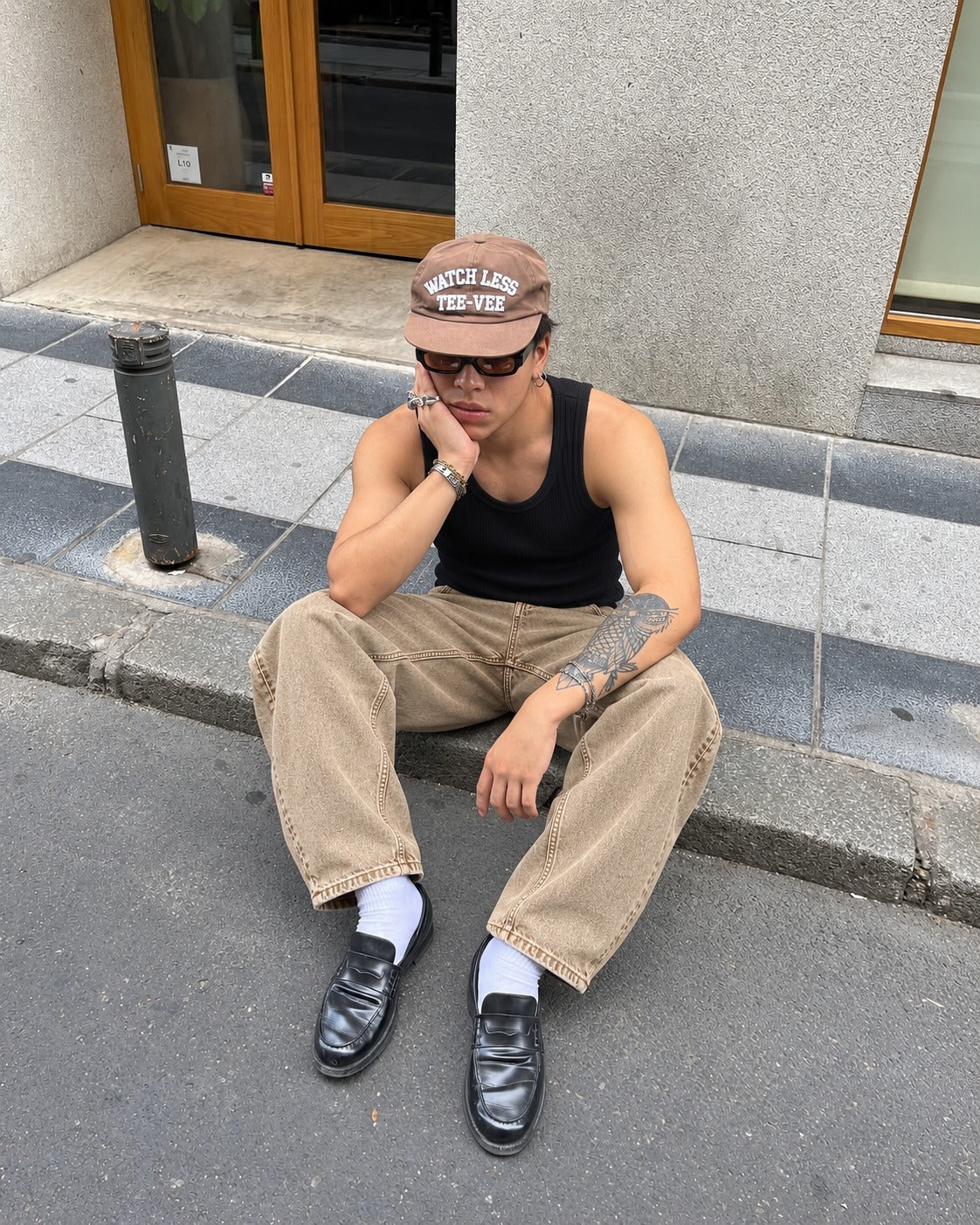 Modelo sentado en la calle con musculosa negra y pantalon pigmentado beige