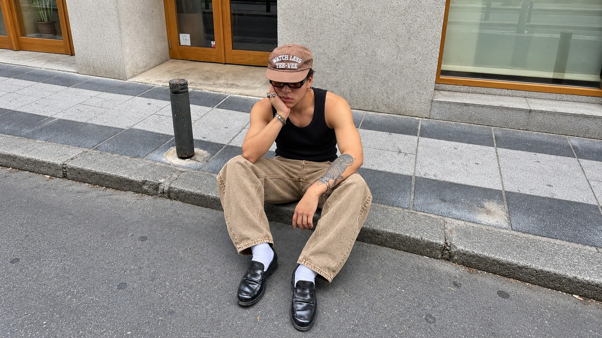 Modelo sentado en la calle con musculosa negra y pantalon pigmentado beige